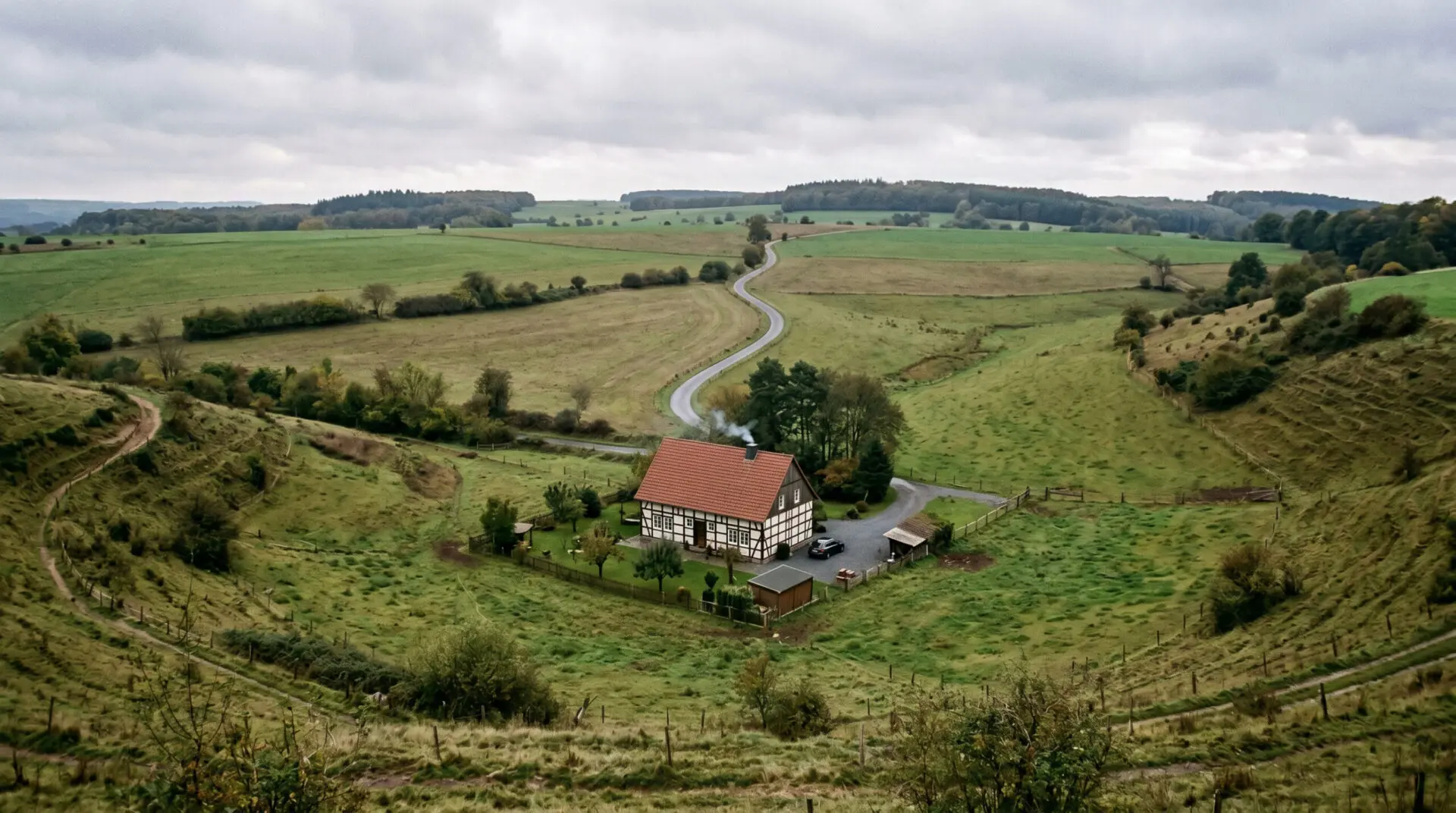 Einsames Einfamilienhaus in einer Geländesenke umgeben von weiten, unbebauten Wiesen im Außenbereich.