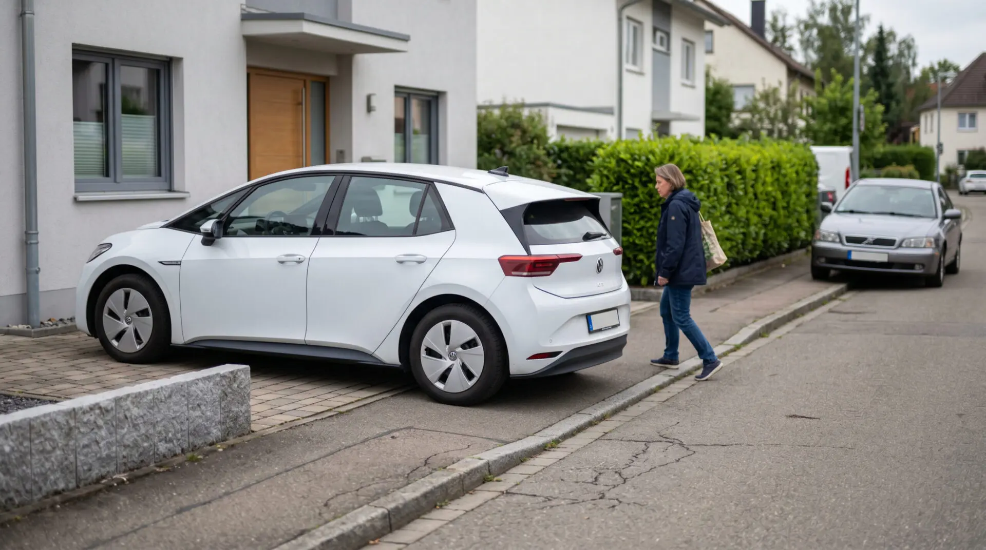 Ein Elektroauto ragt hinten über den Bordstein auf einen schmalen Gehweg, ein Fußgänger muss ausweichen.